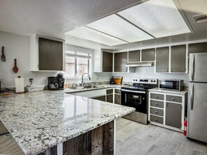 Una cocina moderna con encimera de granito, electrodomésticos de acero inoxidable y un amplio ventanal.