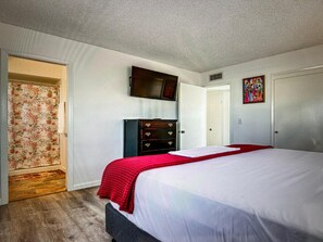 Un dormitorio con cama, cómoda, televisor en la pared y una puerta.