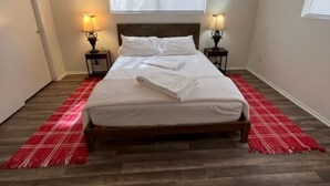 A bedroom with a wooden bed, two bedside lamps, a red plaid runner, and a window with blinds. - Casa Moldavia (Bullhead City)