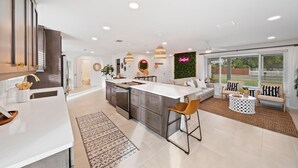 Una cocina moderna con una isla central, taburetes de bar y un comedor con una mesa redonda y sillas.