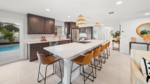 Una cocina moderna con una isla grande, armarios de madera oscura e iluminación colgante.
