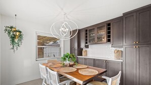 Una cocina moderna con armarios oscuros, una mesa de comedor de madera y sillas blancas.