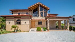 A two-story house with a stone facade, a wooden deck, and a paved driveway.