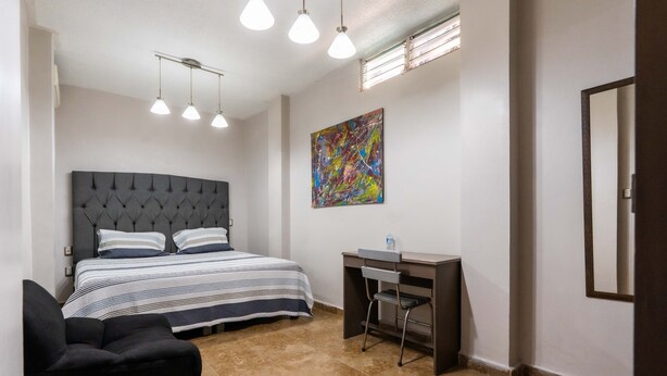 A bedroom with a bed, a desk, and a chair. There is a painting on the wall and a window with blinds. - Hotel Boutique 5ta avenida (Córdoba)