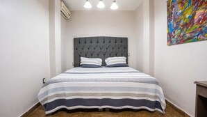 A neatly made bed with striped bedding and a tufted headboard in a room with white walls and a colorful abstract painting. - Hotel Boutique 5ta avenida (Córdoba)