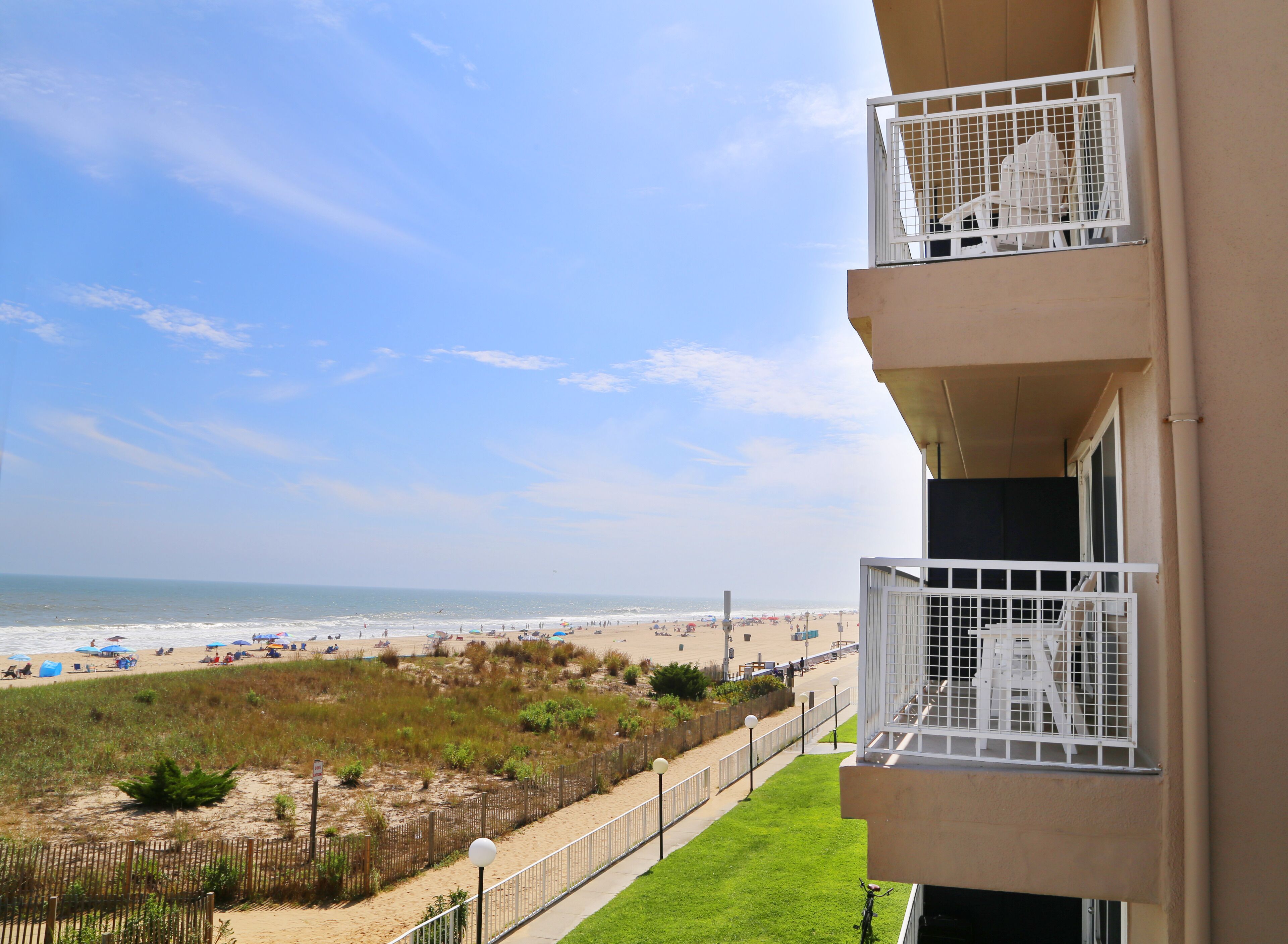 Un balcon donnant sur une plage, un espace clos avec de l’herbe et un ciel dégagé.