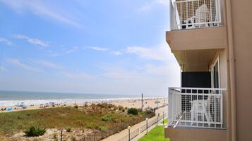 A balcony with a view of a beach, a fenced area with grass, and a clear sky.