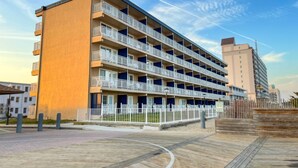 A multi-story hotel with balconies, a wooden boardwalk, and a clear sky. - Dunes Suites Oceanfront (Ocean City)