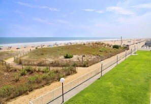 A beach with a fenced area, a grassy lawn, and a pathway. - Dunes Suites Oceanfront (Ocean City)