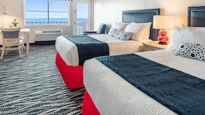 A hotel room with two beds, a desk, a chair, a lamp, and a view of the sea. - Dunes Suites Oceanfront (Ocean City)