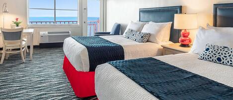 Een hotelkamer met twee bedden, een bureau, een stoel, een lamp en uitzicht op zee.