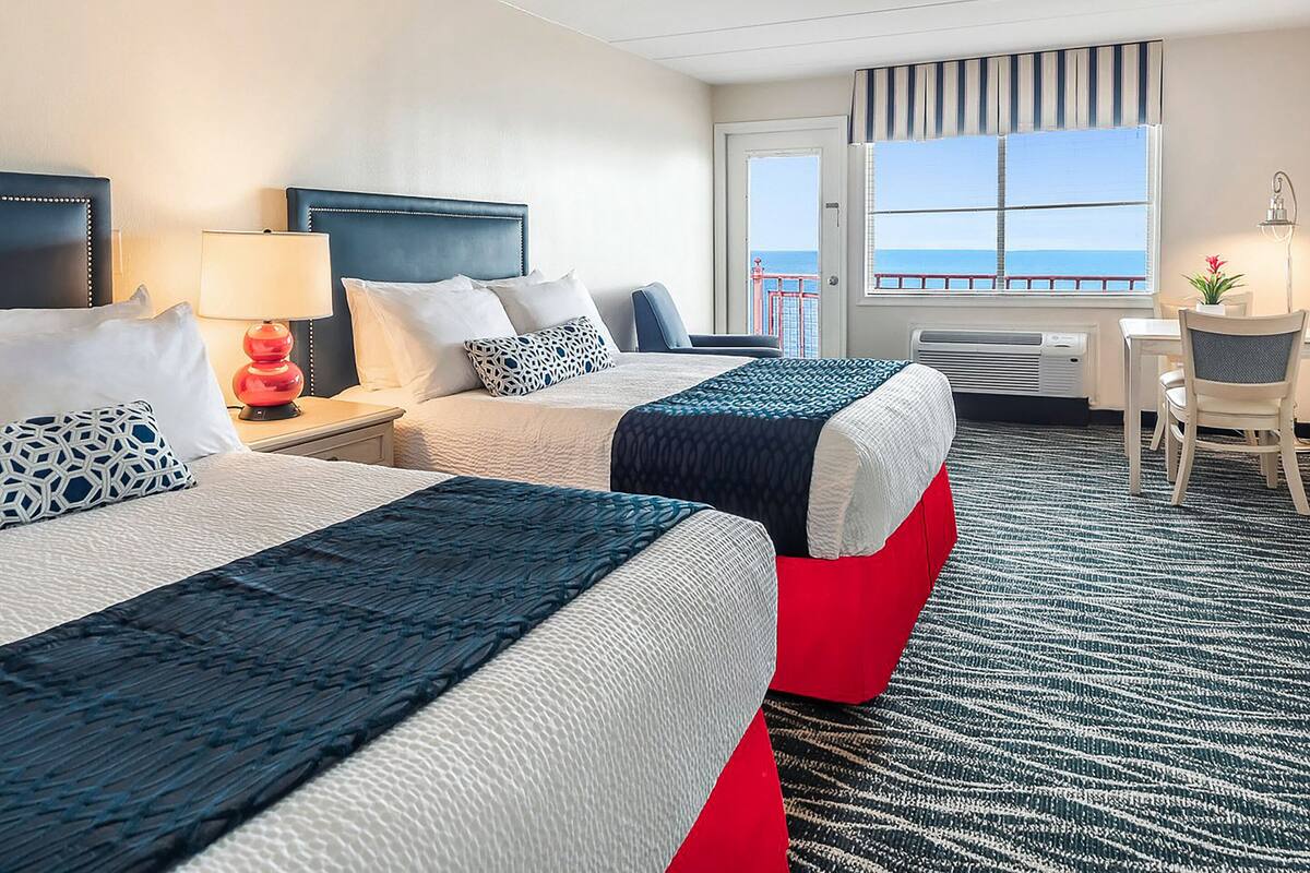 A hotel room with two beds, a desk, and a view of the sea.