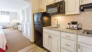A compact hotel kitchen with white cabinetry, a black refrigerator, a microwave, and a sink. - Dunes Suites Oceanfront (Ocean City)