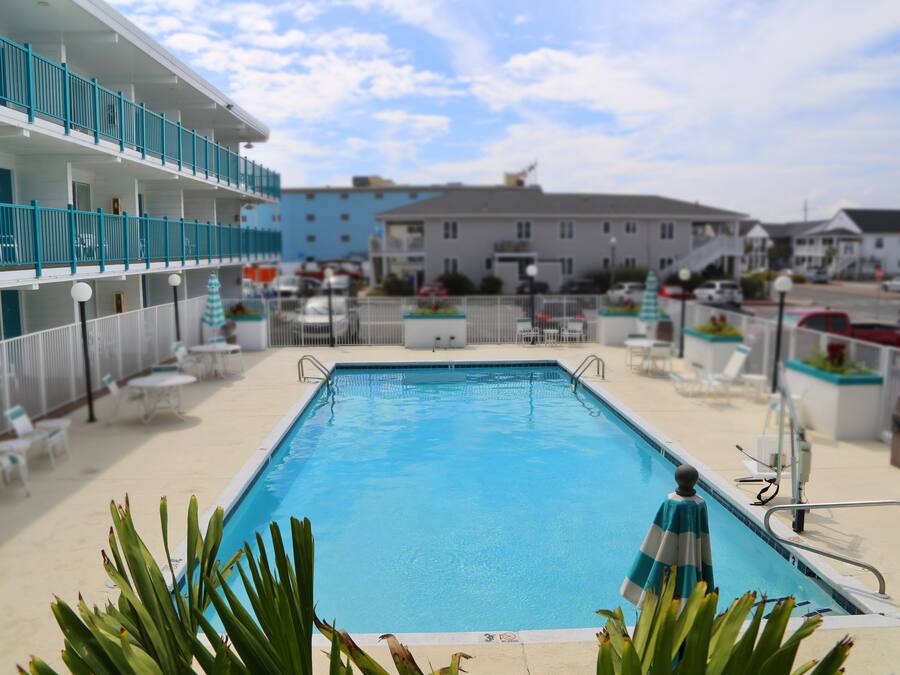 A swimming pool with a blue water feature, surrounded by lounge chairs and a building with balconies.
