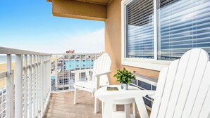 A balcony with white chairs and a small table, overlooking a beach and buildings. - Dunes Suites Oceanfront (Ocean City)