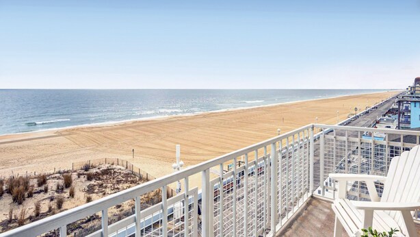 A beach view from a balcony with a railing, a sandy beach, and a pier extending into the water. - Dunes Suites Oceanfront (Ocean City)