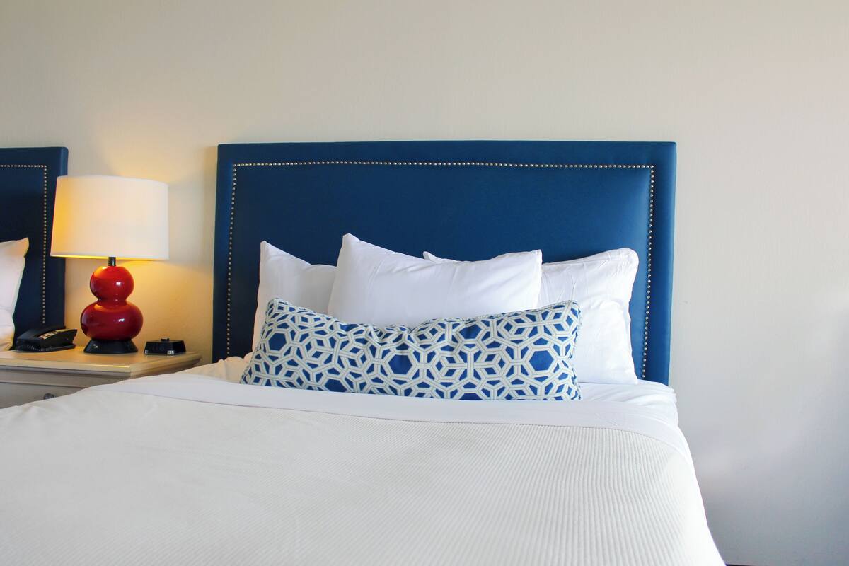 A hotel room with a bed, a nightstand with a lamp, and a mirror.