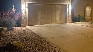 Un garage bien éclairé, doté d’une façade en pierre, d’une allée en béton et d’un espace paysager agrémenté de rochers et d’arbustes.