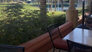 Une terrasse extérieure offrant une vue sur un terrain de golf, des palmiers, ainsi qu’un espace salon abrité avec des chaises et une table.