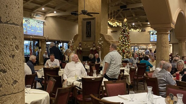L’intérieur du restaurant se caractérise par de hauts plafonds, des colonnes en pierre et un lustre central. Les tables sont dressées avec des nappes blanches et des chaises rouges.