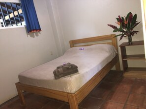 A single bed with a wooden frame and a white mattress in a room with tiled flooring.
