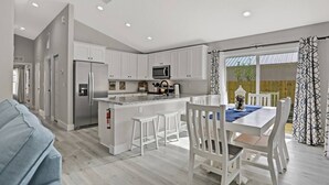 Une cuisine moderne avec des meubles blancs, un îlot central et un coin repas comprenant des chaises et une table, le tout dans des tons blancs.