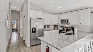 Une cuisine moderne avec des meubles blancs, des appareils en acier inoxydable, des comptoirs en granit et un îlot central doté de tabourets de bar.