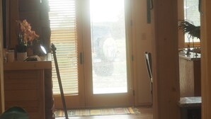 A wooden interior with a sliding glass door leading outside, a small table with a vase of flowers, and a hanging light fixture.