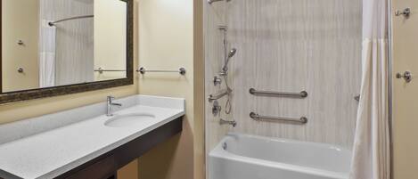 A bathroom with a sink, mirror, and bathtub.