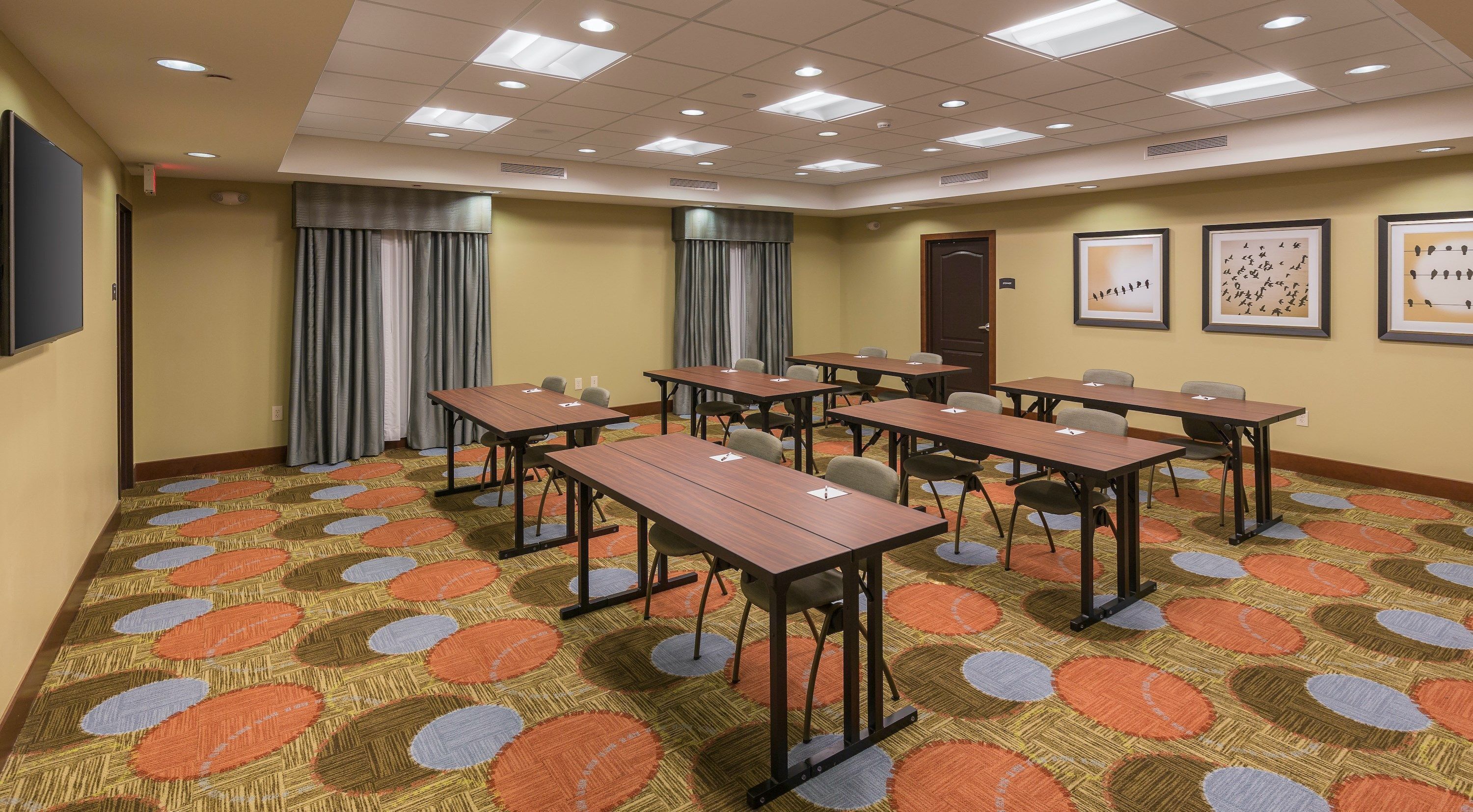 A conference room with multiple tables and chairs, a patterned carpet, and ceiling lights.