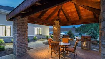 Eine Terrasse im Freien mit einer Holz-Pergola, Steinpfeilern, einem Grill und einem Tisch mit Stühlen.