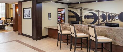 A reception area with a marble counter, three bar-style chairs, a bookshelf, and a large wall mural of a bridge.
