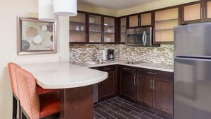 A modern kitchen with dark wood cabinets, a stainless steel refrigerator, a microwave, and a tiled backsplash. - King Studio | Free Breakfast, Shared Hot Tub, Pool (Canton)