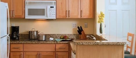 Cozinha com armários de madeira, micro-ondas, cafeteira e uma pequena ilha com suporte para facas.