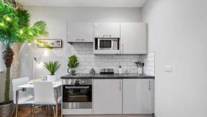 A modern kitchen with white cabinets, a microwave, an oven, and a dining area with a white table and chairs. - Luxury 1bed Studio Apt-city Centre-wifi-parking (Maidstone)