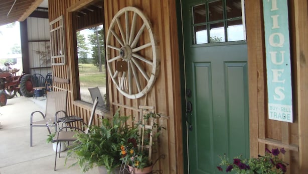 A rustic building with a green door, a large wooden wheel, and a sign reading "ANTIQUES".