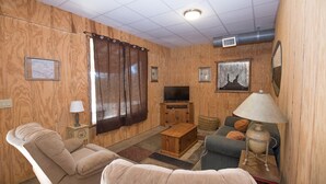 A cozy living room with wooden paneling, a television, a sofa, a loveseat, a lamp, and a small table.