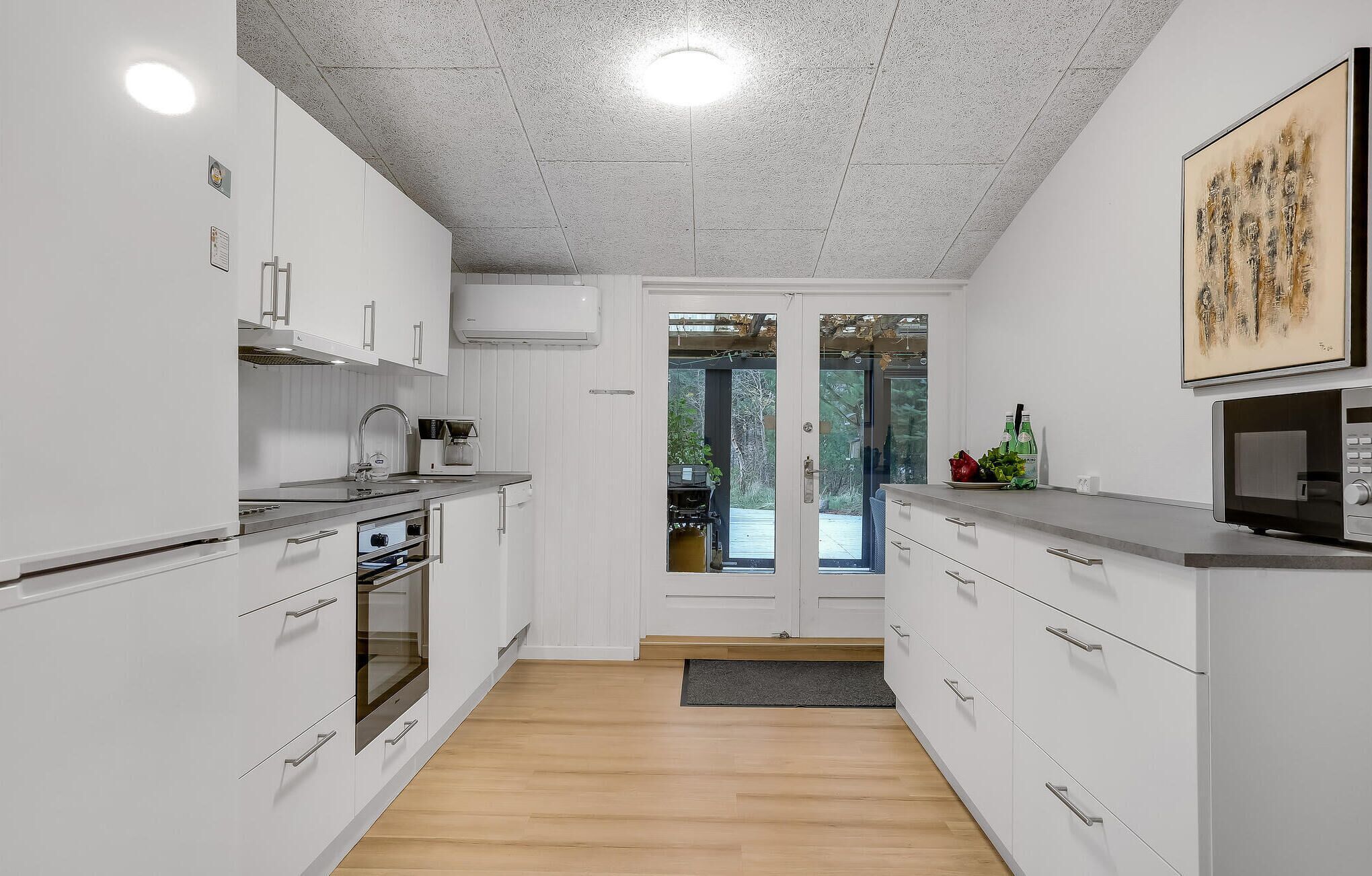 A modern kitchen with white cabinets, stainless steel appliances, and a wooden floor.