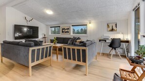 Ett modernt vardagsrum med en platt-TV, grå soffor, ett träbord och ett skrivbord med en dator.