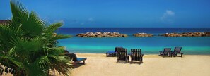A beach with clear turquoise water, a sandy shore, and several wooden lounge chairs. - Fabulous Canal Front Villa, 37 ft Dock and 8-person hot tub (key colony beach)