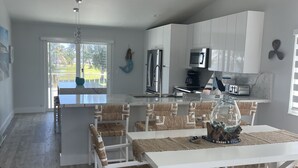 Una cucina moderna con mobili bianchi, elettrodomestici in acciaio inossidabile e un'area pranzo con tavoli bianchi e sedie in vimini.