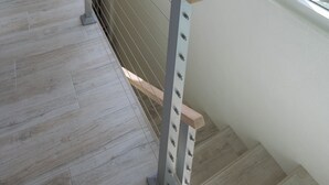 Una scala in legno con ringhiera in metallo che conduce a un balcone con ampie finestre affacciato su una marina con barche e palme.
