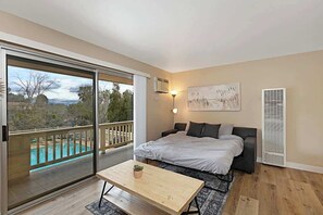 Un dormitorio con cama, una mesa, un cuadro y vistas a una piscina y árboles.