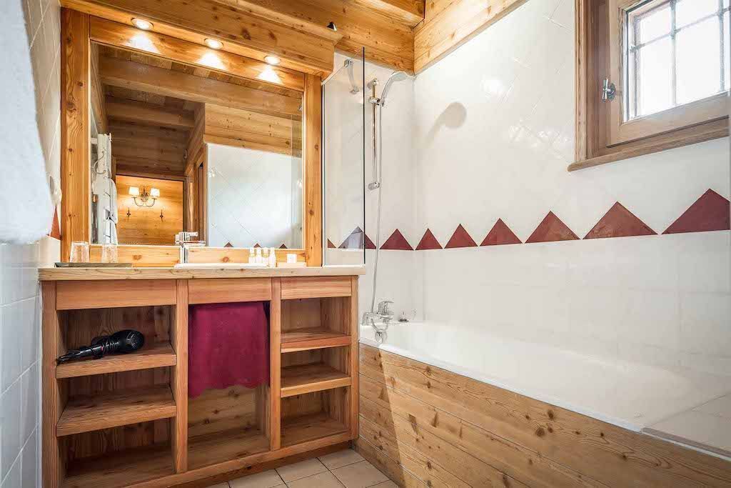 Ein Badezimmer einer Holzhütte mit einem großen Spiegel, Holzregalen, einer Badewanne und einer Dusche.