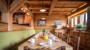 A wooden dining area with a long table set for breakfast, wooden walls, and a bench.