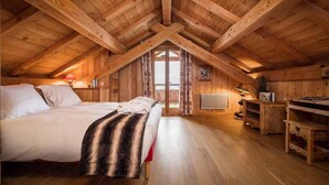 A cozy attic bedroom with a wooden ceiling, a bed, a desk, and a window.