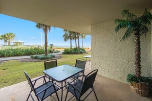 An outdoor patio with a table and chairs, a potted plant, and a view of the beach and palm trees. - Seaside 4108- Direct Gulf Front Unit, Charming First Floor Location, Tons of Family Amenities (Orange Beach)