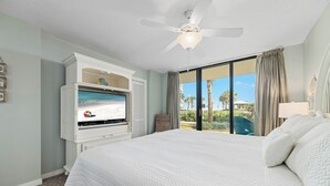 Habitació d'hotel amb un llit gran, una televisió sobre un moble blanc i vista a les palmeres i la platja per la finestra.