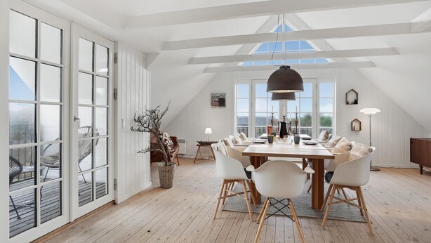 Un amplio comedor con techo alto y ventanas grandes, que incluye una mesa de madera y sillas blancas.