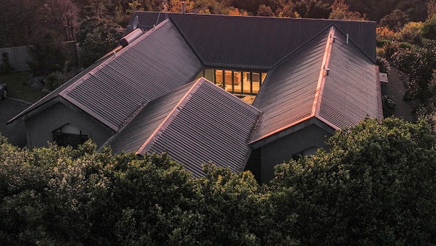 Et moderne hus med skråt tag, omgivet af frodig vegetation og med udsigt over en dal.